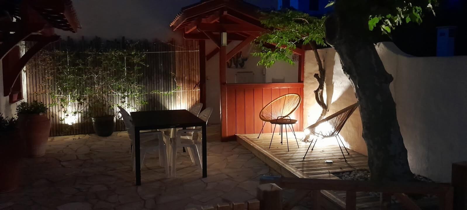 An outdoor patio area with a wooden table and chairs, a hammock, and a small wooden structure.