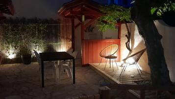 An outdoor patio area with a wooden table and chairs, a hammock, and a small wooden structure.