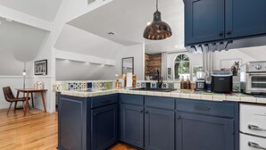 A modern kitchen with dark blue cabinets, a white countertop, and a hanging pendant light. - Downtown Wimberley Treehouse | Hot Tub Under Stars (Wimberley)