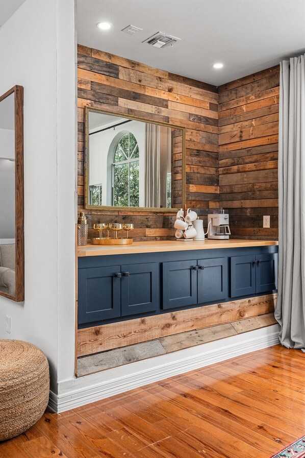 A bathroom with a wooden wall, a large mirror, and a dark blue cabinet.