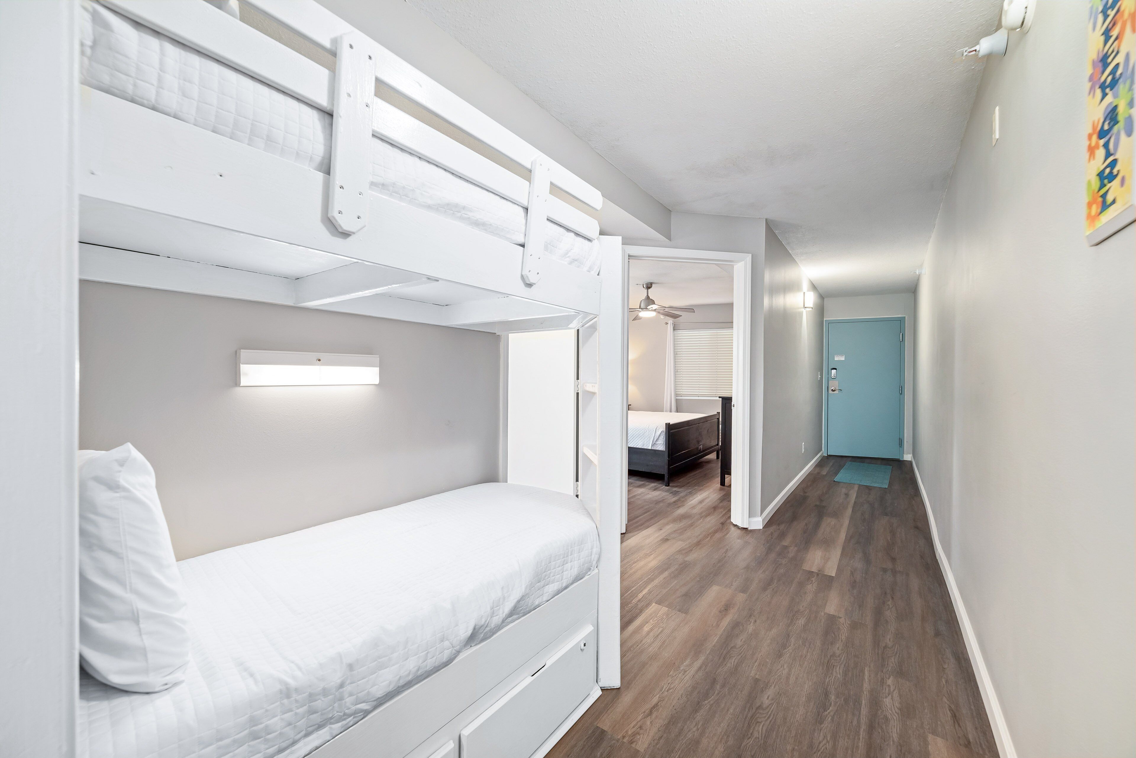A room with bunk beds, a door, and a hallway leading to another room.