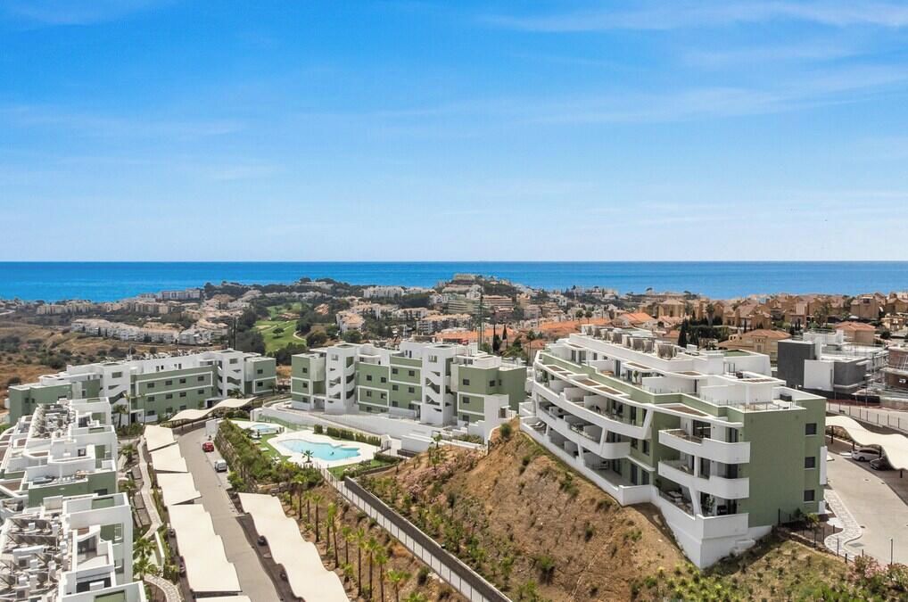 A coastal residential area with modern buildings, a swimming pool, and a view of the sea.