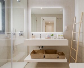 Un baño moderno con cabina de ducha de vidrio, un tocador blanco con espejo y cestas de almacenamiento debajo.