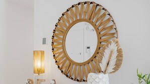 Een houten tafel met een witte vaas en decoratieve letters die 'SEA' vormen, op een muur met een grote spiegel en een wandlamp.