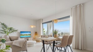 Een moderne woonkamer met een televisie, eethoek en grote ramen voorzien van gordijnen.