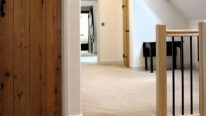 A spacious loft with exposed wooden beams, a large wooden door, and a view of a bedroom through an open doorway.