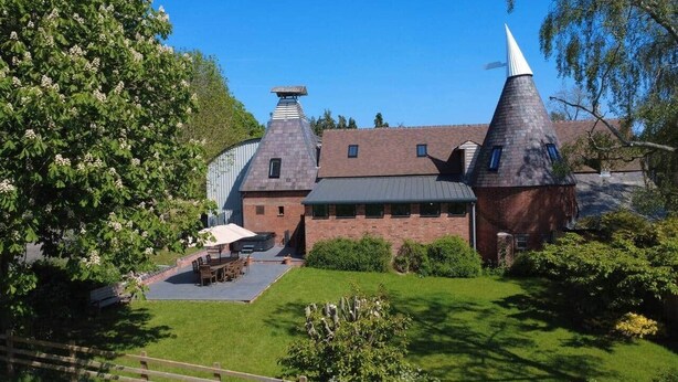A large building with a brick facade, two conical towers, and a paved courtyard with outdoor furniture.