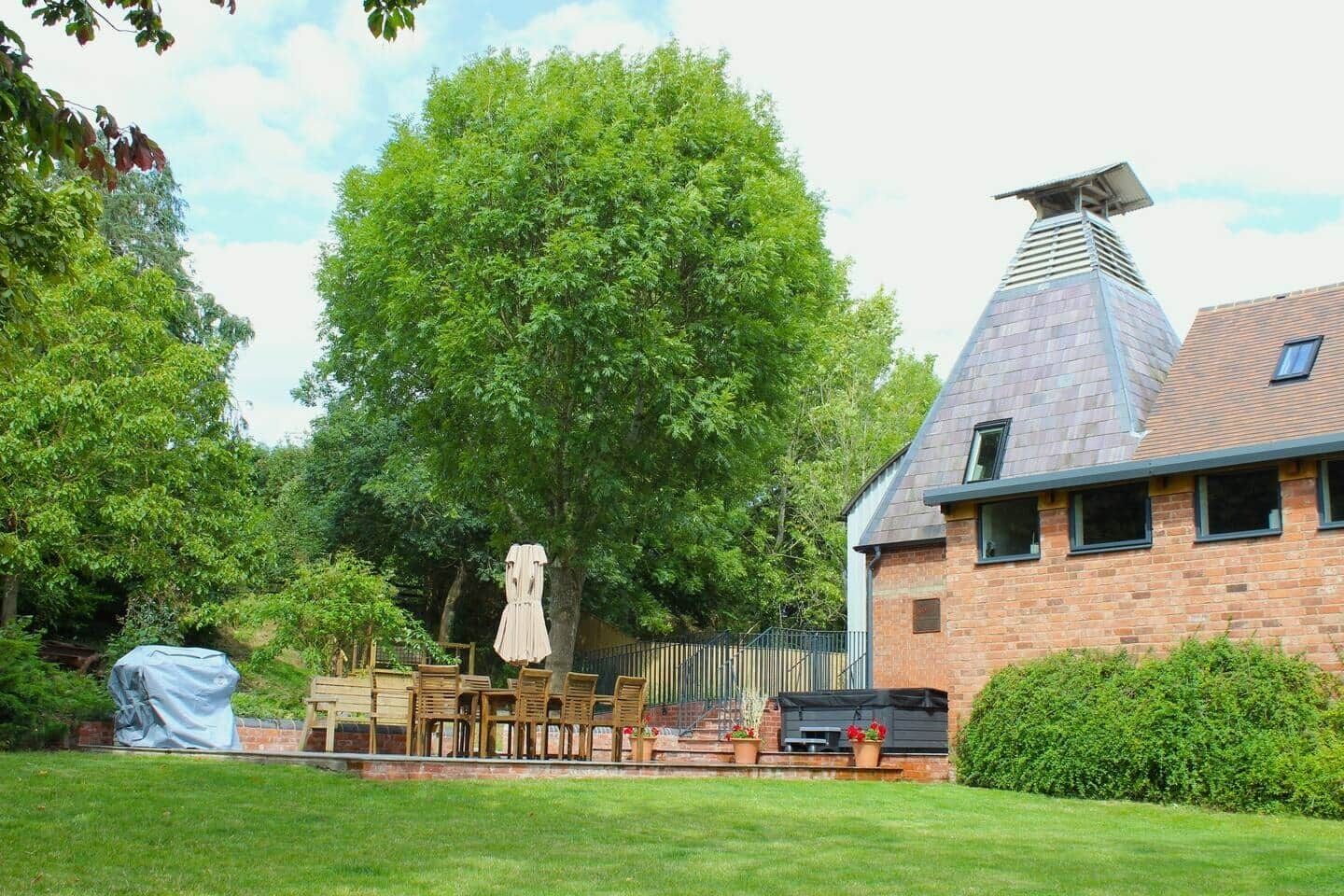 Ein Ziegelhaus mit geneigtem Dach, ein großer Baum im Garten und Gartenmöbel.
