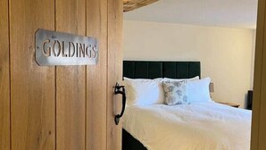 A bedroom with a wooden door labeled 'GOLDINGS,' a bed with white bedding, and a dark headboard.
