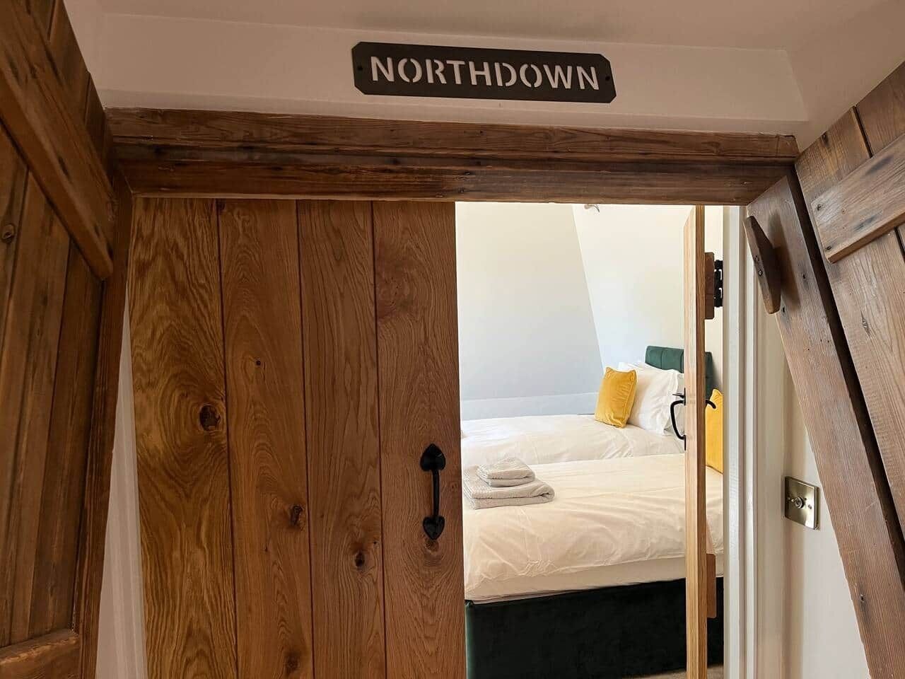 Una puerta de madera con un letrero que dice 'NORTHDOWN' que da a un dormitorio con cama y almohadas.
