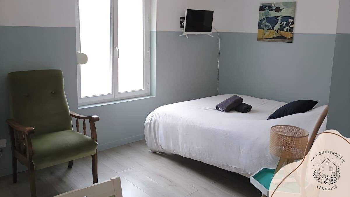 Une chambre avec un lit, une chaise, un téléviseur et un tableau accroché au mur.