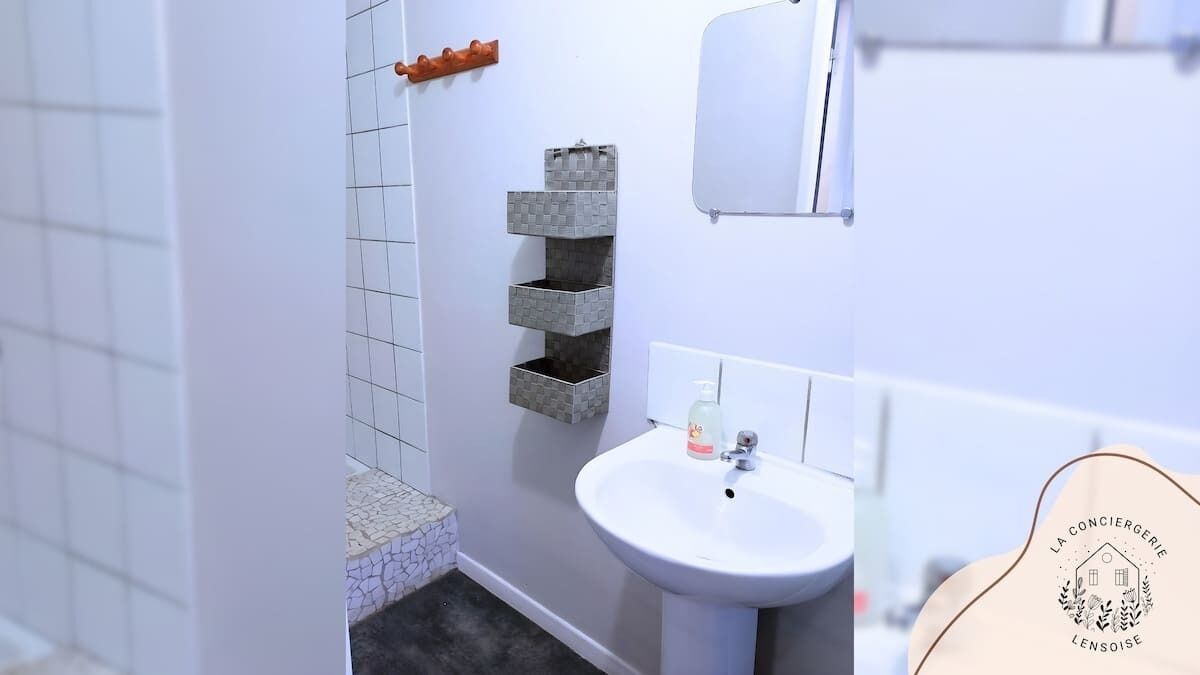Une salle de bain avec un lavabo blanc, un miroir et un mur recouvert de carreaux.