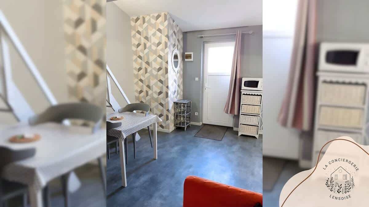 Une pièce comprenant une table à manger, une chaise, une petite table avec une lampe, une armoire et une fenêtre avec des rideaux.