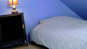 A small, dimly lit room with a slanted ceiling, a single bed with a patterned blanket, a bedside table with a lamp, and a wooden floor. - LES COMBLES DE PIERRE 6, Bollaert, Fac, 1pers, parking (Lens)