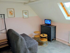 Une pièce avec un lit en mezzanine, un petit bureau avec un écran d’ordinateur, deux tableaux encadrés au mur et une lucarne.