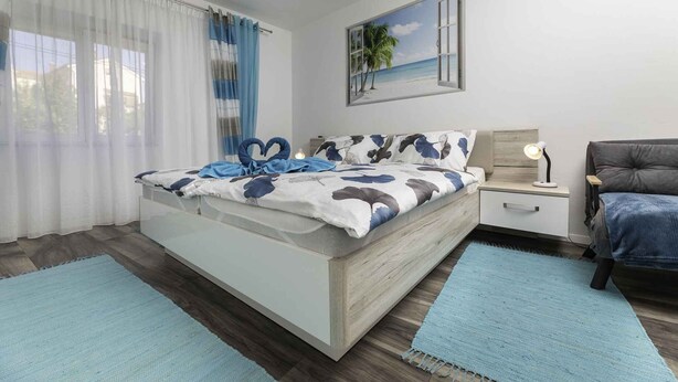 Een moderne slaapkamer met een bed, nachtkastje, lamp en uitzicht op het strand door een raam.