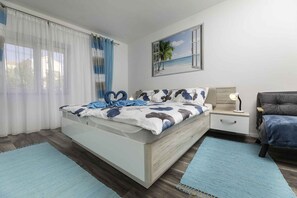 A modern bedroom with a bed, a nightstand, a lamp, and a view of the beach through a window.