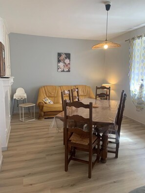 A dining area with a wooden table, chairs, a sofa, a small side table, and a hanging light fixture. - Chez Mamie Gigi - DIENVILLE (DIENVILLE)