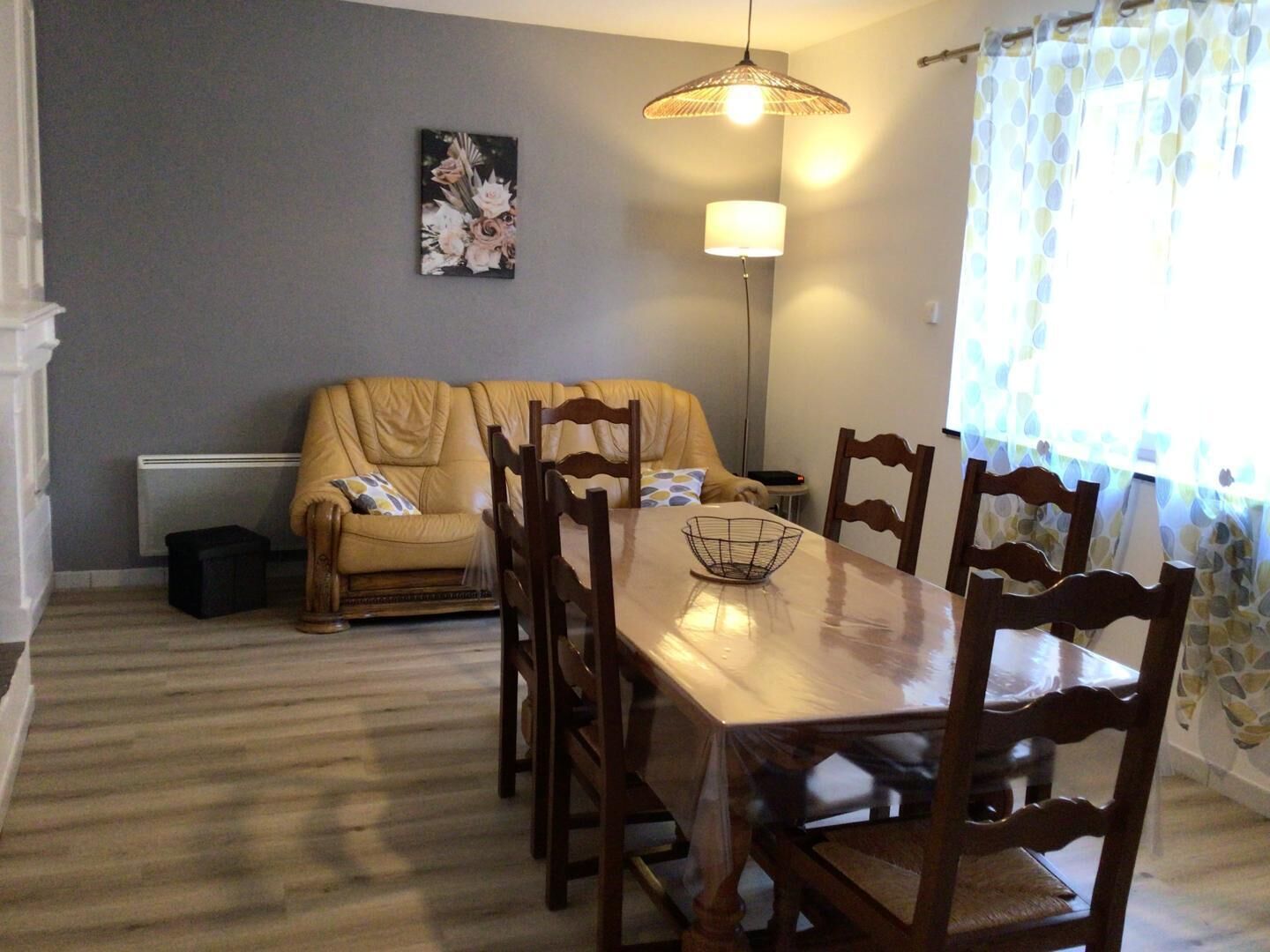 A dining area with a wooden table, chairs, a floor lamp, and a sofa.