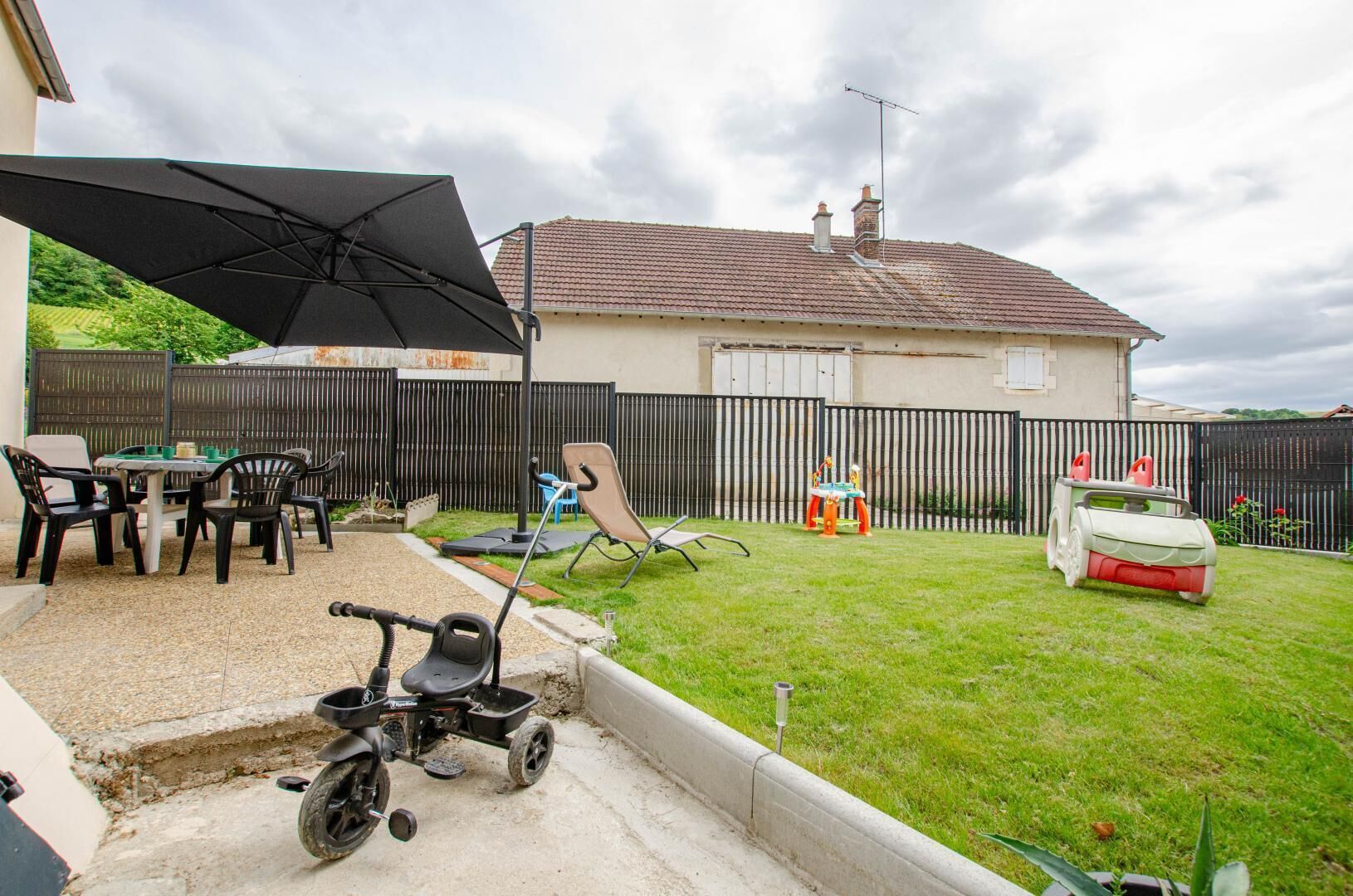 A backyard with a patio table, chairs, a children's playset, and a tricycle.