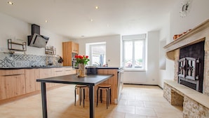 A modern kitchen with a central island, wooden cabinets, and a stone fireplace.