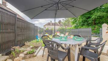 Eine Terrasse im Freien mit Tisch für vier Personen, umgeben von Stühlen, unter einem großen Sonnenschirm.