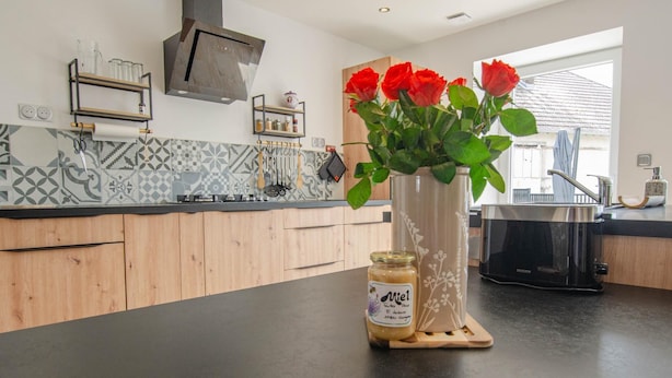 A modern kitchen with a black countertop, wooden cabinets, a stainless steel range hood, and a vase with red roses.