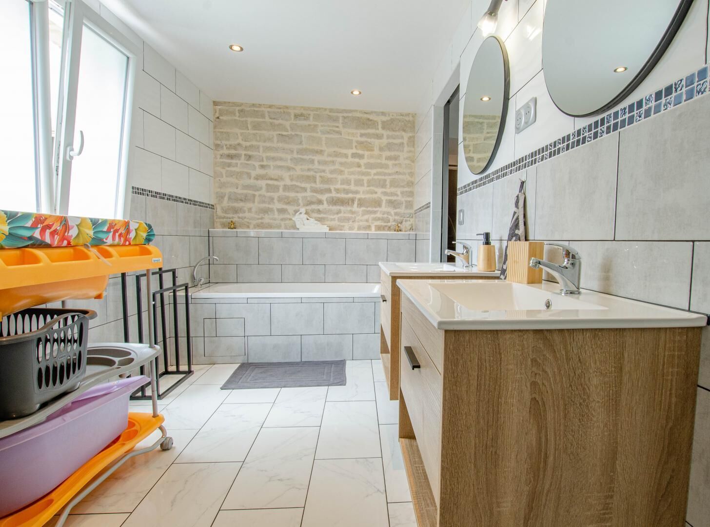 Un baño moderno con pared de piedra, una bañera, dos lavamanos y un tocador.