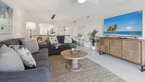 A modern living room with a gray sofa, a round coffee table, and a wooden cabinet with a TV. - Beachside Ground Floor Condo | Steps to the Beach, Heated Pool & Private Patio 🌴 (Cocoa Beach)