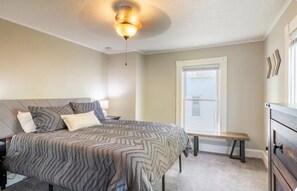 A bedroom with a bed, bedside tables, a bench, a dresser, a ceiling fan, and a window with blinds.