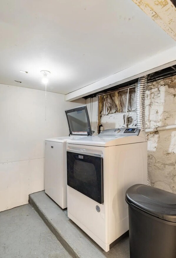 A compact laundry room with a washing machine, dryer, and a trash bin.