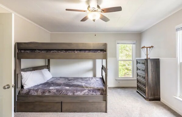 Una cama litera con cabecera, ventana con vistas y ventilador de techo.