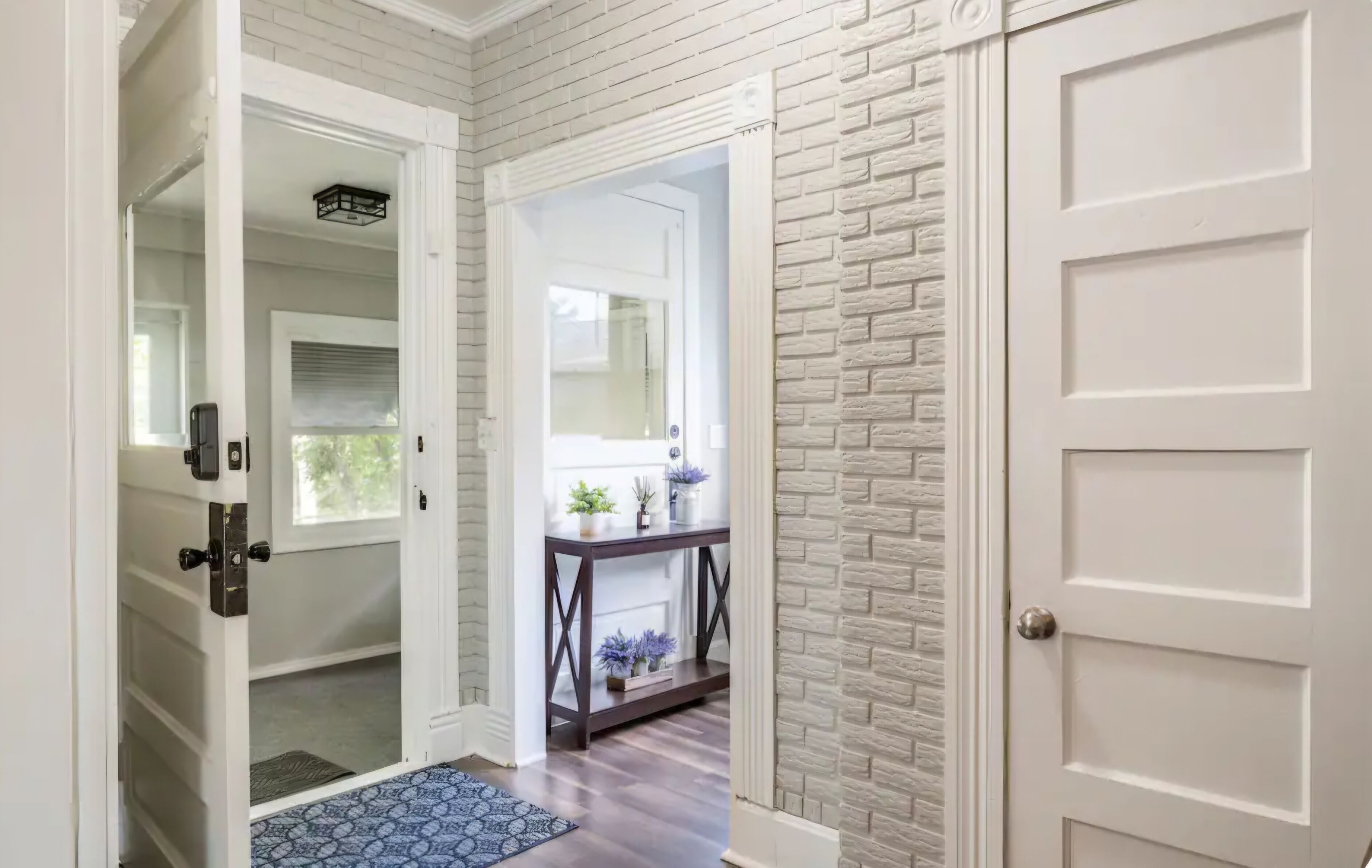 A hallway with a white door, a white wall with a brick pattern, and a small table with plants.