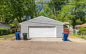 A single-story garage with a white garage door, two trash bins, and a clear sky in the background.