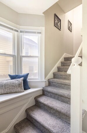 A staircase with carpeted steps leading to a landing with a window seat.