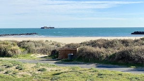 A beach with a lighthouse, a wooden fence, and a trash bin.
