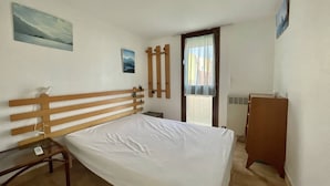 A bedroom with a wooden bed frame, a small bedside table, a wardrobe, and two wall-mounted paintings.