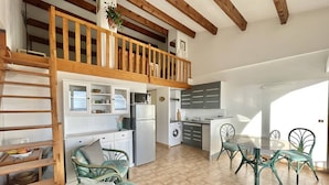 A spacious kitchen with a loft bedroom, a dining area with chairs, and a washing machine.