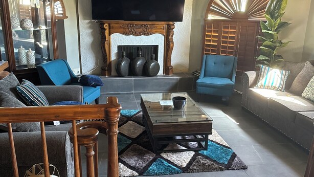 A spacious living room with a fireplace, a flat-screen TV mounted above it, and a ceiling fan. - Beautiful Vacation Home with Pool (Yuma)