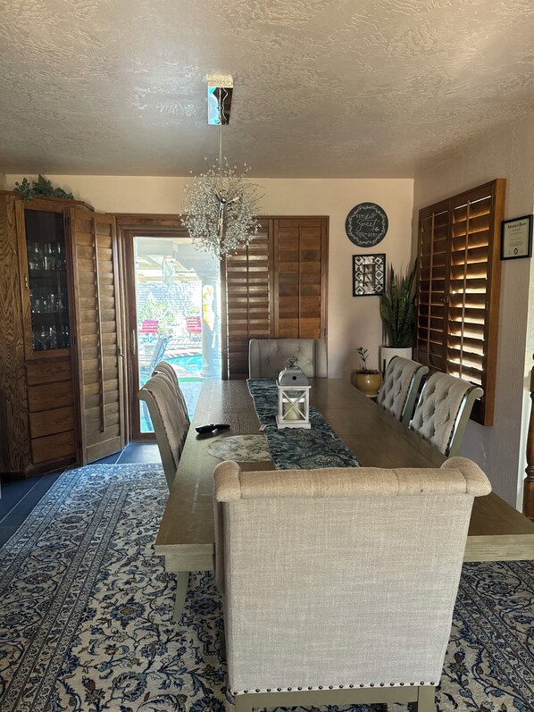 A dining area with a wooden table, upholstered chairs, a chandelier, and patterned rugs.
