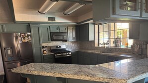 A kitchen with granite countertops, a stainless steel refrigerator, a microwave, and a stove. There are two brown bar stools in front of the island. - Beautiful Vacation Home with Pool (Yuma)
