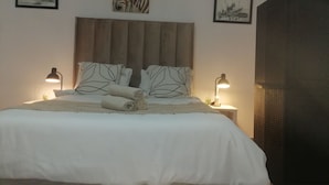 Un dormitorio con una cama grande, dos lámparas de noche, un cabecero y dos cuadros enmarcados en la pared.