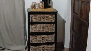 Una habitación con televisión montada en la pared, un armario de madera con cestas de mimbre, una cafetera y una puerta de madera.