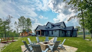 Une maison moderne dotée d’une terrasse en pierre et de chaises Adirondack.