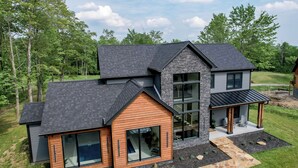 Une maison moderne à deux étages, dotée d’une façade en pierre, de grandes fenêtres et d’un porche abrité.