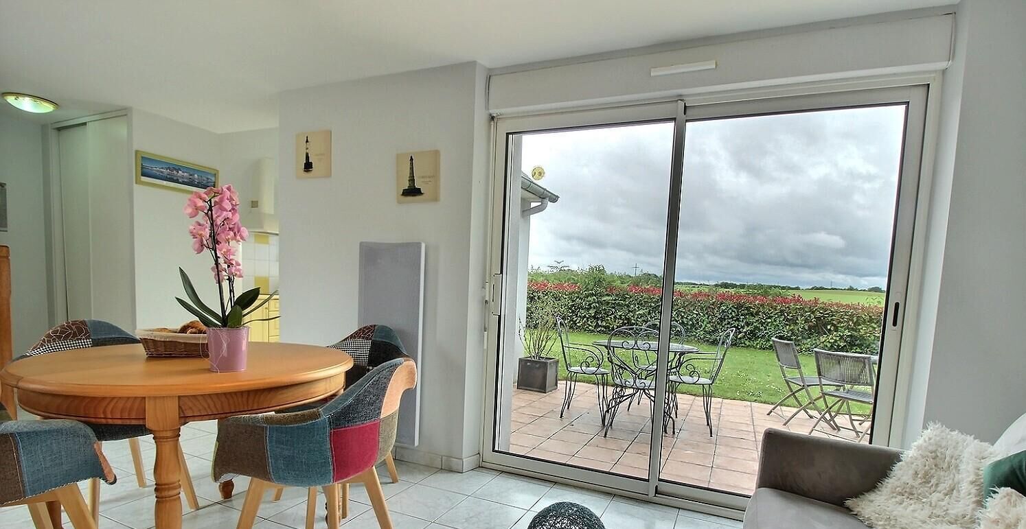 A dining area with a round table and chairs, a potted plant, and a view of a garden through a sliding glass door.