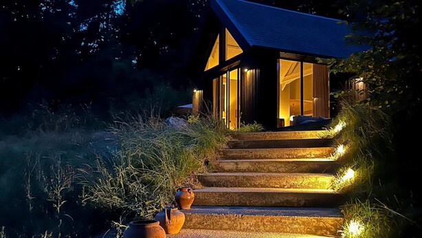 A modern house with a glass facade, a wooden exterior, and a stone staircase leading to the entrance.