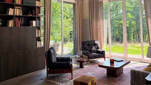 A spacious living room with a large bookshelf, a comfortable armchair, a small ottoman, and a coffee table.