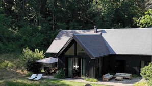 A modern house with a sloped roof, a covered patio with outdoor furniture, and a fire pit area.