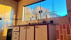 A kitchen with a large window, cabinets, a stove, and a sink.